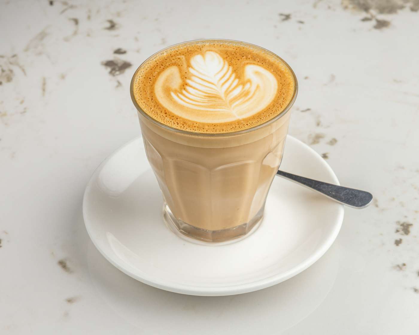 A barista-poured latte in a faceted glass